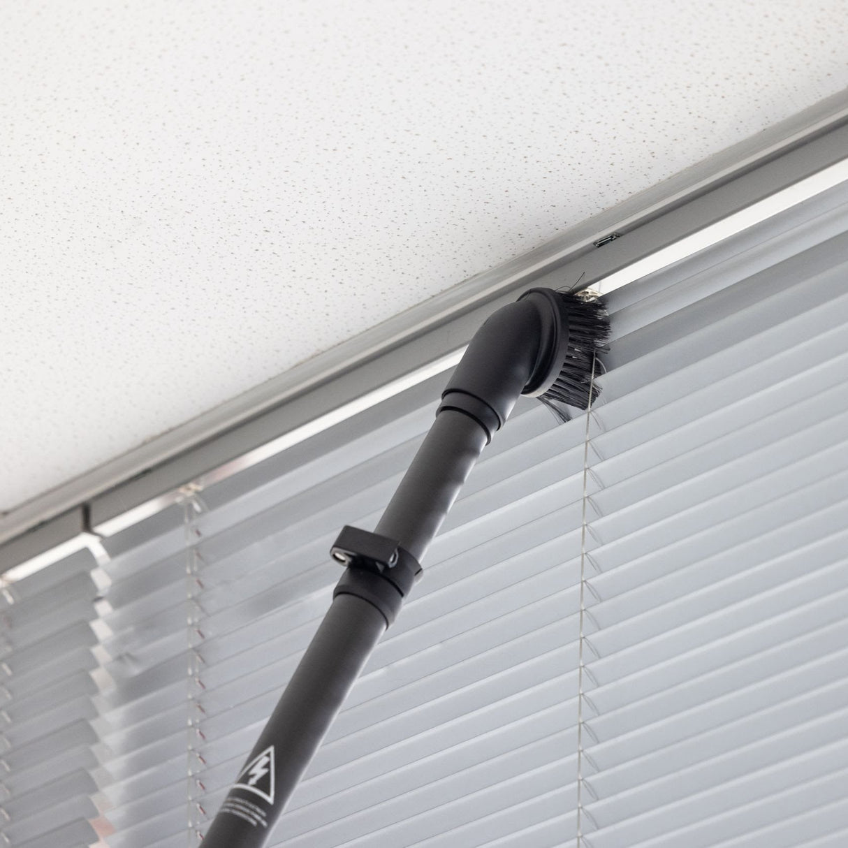 Vacuum cleaning a window blind with a black vacuum attachment.