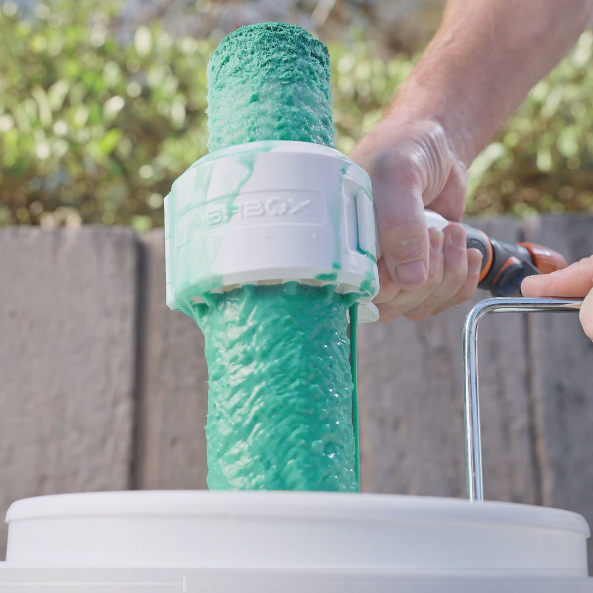 A person using a paint roller attachment connected to a hose, roller covered in paint