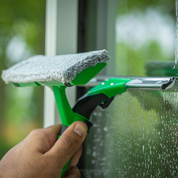 Person cleaning a window with a green squeegee