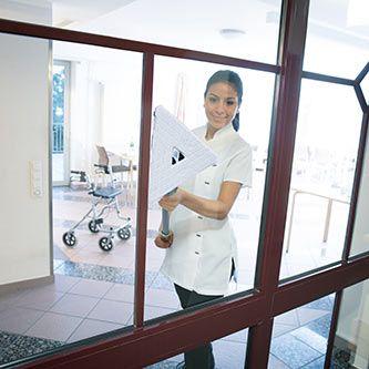 Woman cleaning a glass door with a white cloth in a modern building.