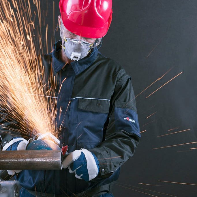 Person wearing a red helmet and protective gear, using a power tool with sparks flying.