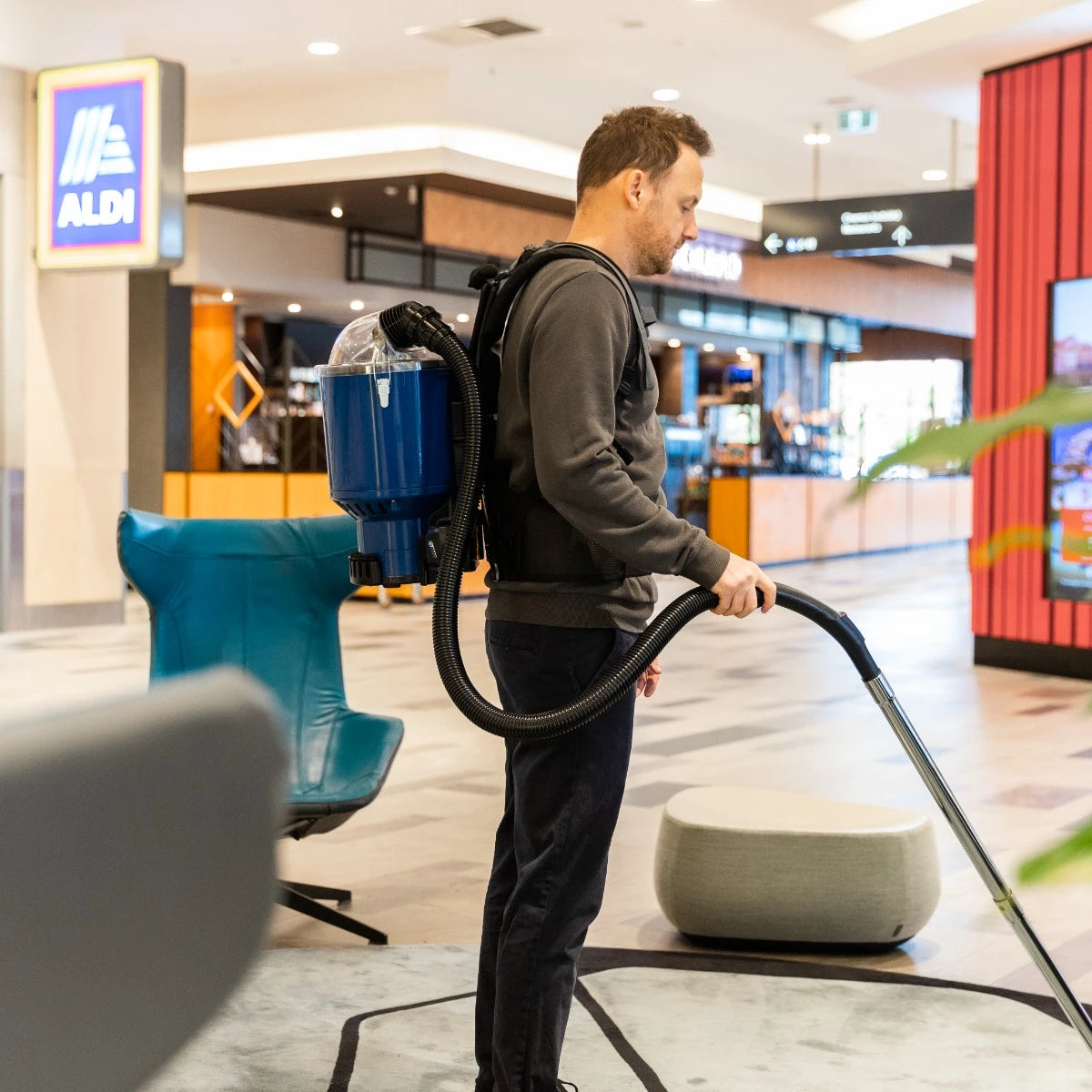 Person using a backpack vacuum cleaner in a shopping mall.
