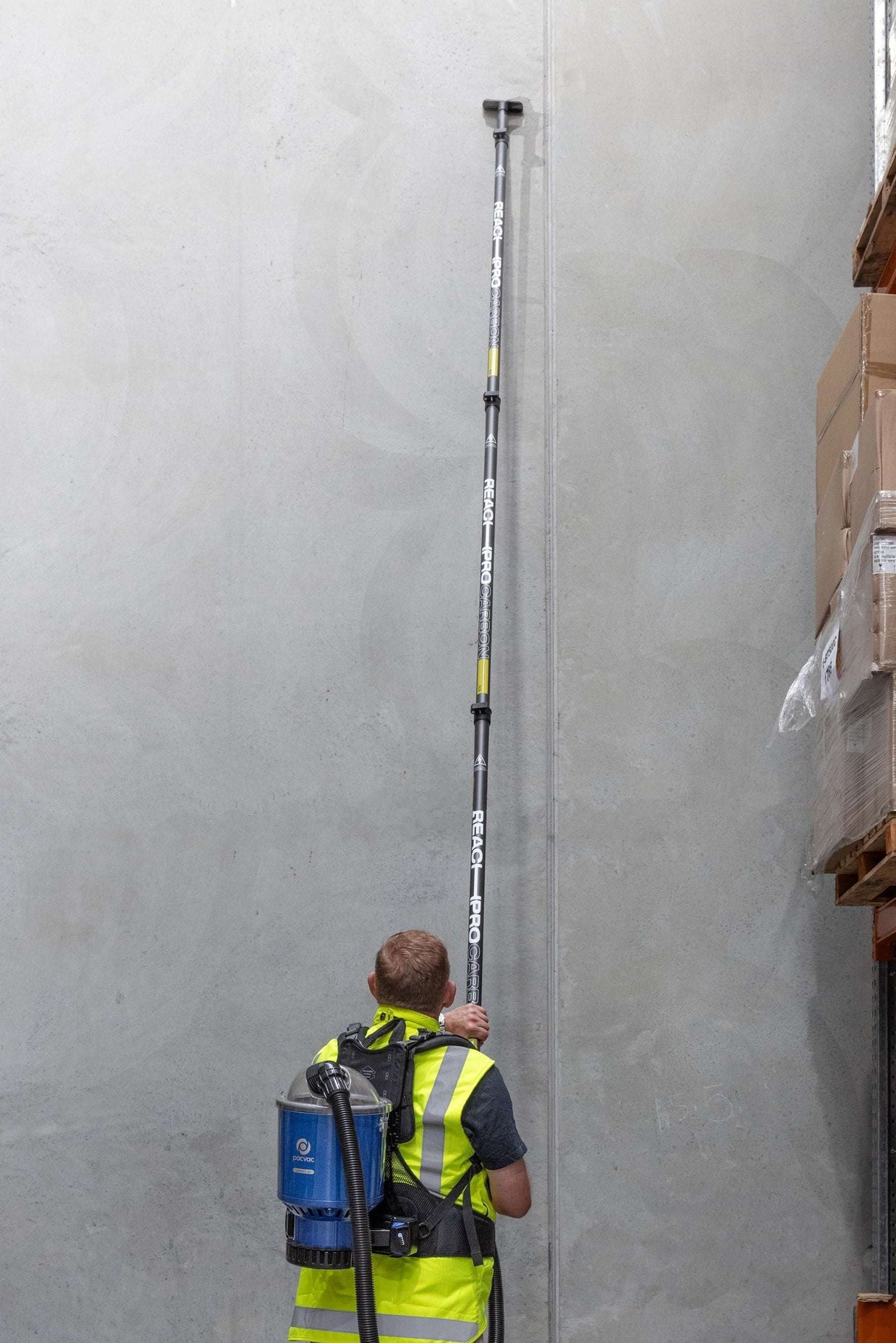 Person in a warehouse using a long measuring device against a wall.