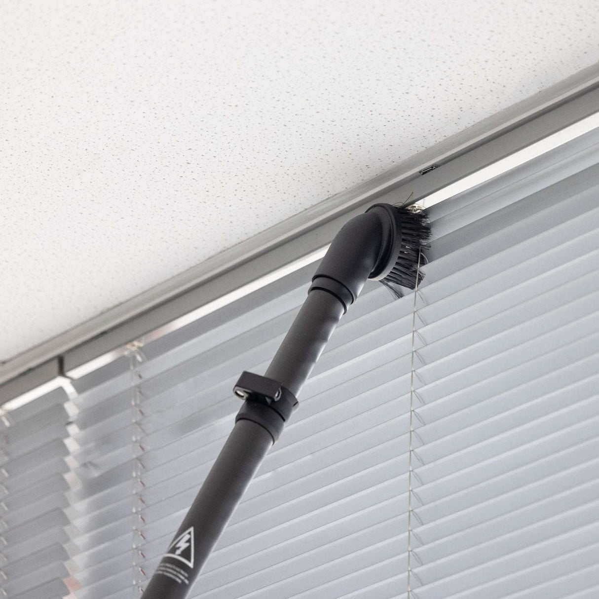 Vacuum cleaning a window blind with a black vacuum attachment.