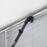 Vacuum cleaning a window blind with a black vacuum attachment.