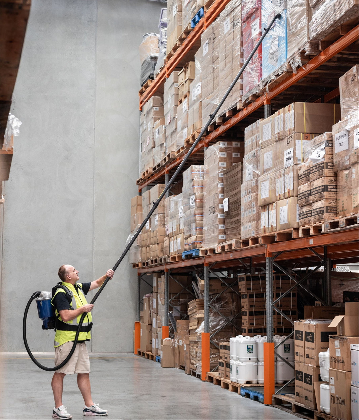 Person using a long-handled tool to interact with items on high shelves in a warehouse.