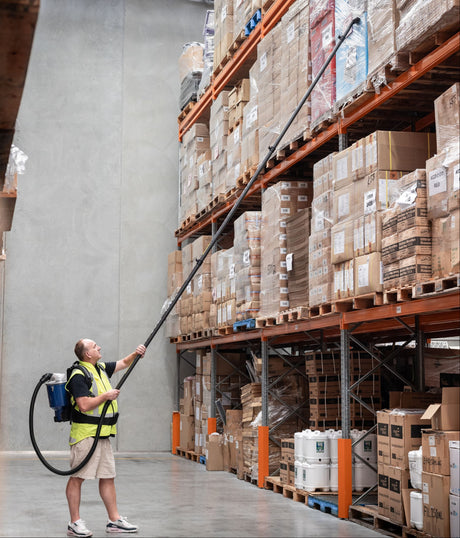 Person using a long-handled tool to interact with items on high shelves in a warehouse.