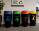 Four colored recycling bins labeled for different waste categories in an office setting.