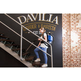 Woman with a backpack walking up stairs in front of a 'Davilia Barber & Barista' sign.