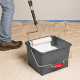 A dark gray plastic paint bucket with a metal handle and a paint roller resting inside, shown on a tan drop cloth 