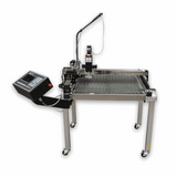 A stainless steel industrial table-top machine with a diamond-plate textured work surface, mounted arm, vertical tool head, and an attached black control console on a wheeled stand, shown on a plain white background.