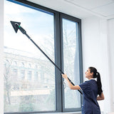 A woman in a navy scrub top uses a stingray extension pole  window cleaning tool with a triangular clean a large office window.